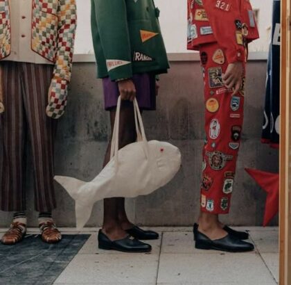 Détail éditorial de trois silhouettes : pantalon rouge entièrement couvert de patches en tissu peint, sac à main blanc en forme de poisson, veste verte, mocassins noirs.