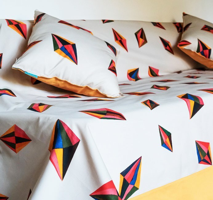 Parure de lit en coton blanc, draps et coussins imprimés du motif Toupies (toupies stylisées peintes à la main en rouge, orange, bleu et noir).