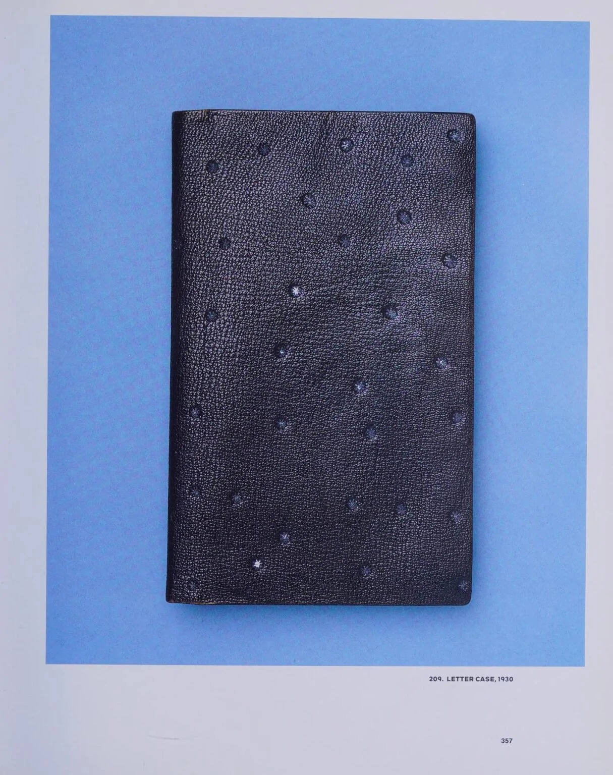 Plain black grained-leather letter case scattered with small blind-stamped six-pointed stars, photographed on a sky-blue background.