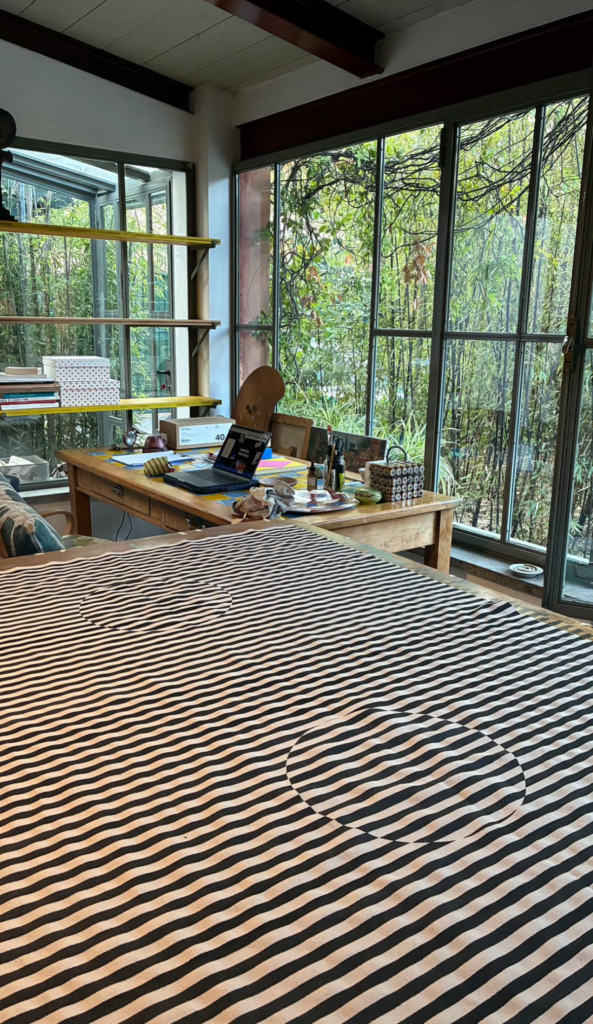 Métrage rayé Spiga drappé sur une grande table dans l'atelier de Zazie, avec bureau, ordinateur portable et baies vitrées donnant sur le jardin.
